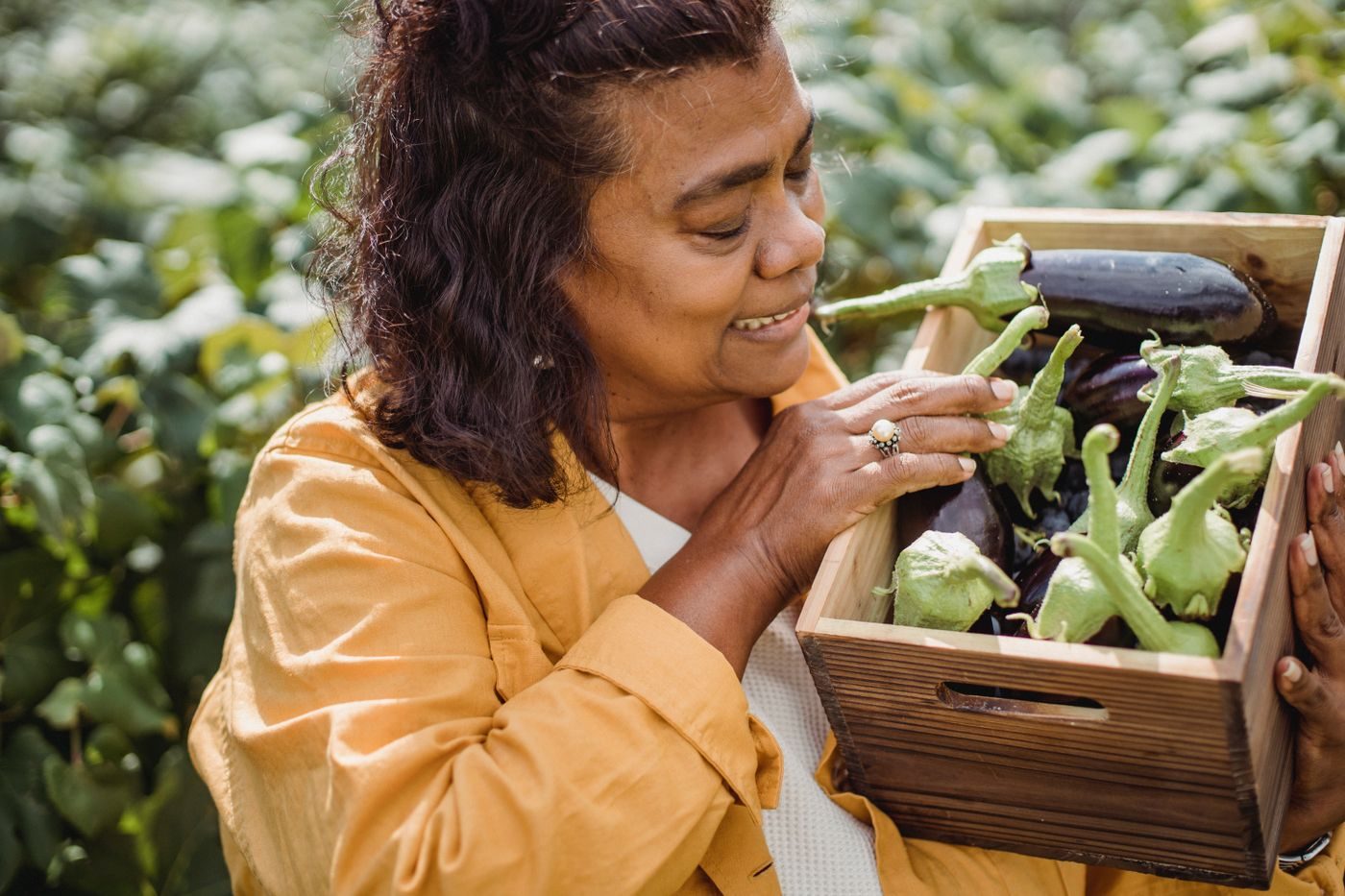 A smiling woman holding a crate of fresh vegetables she has picked at a community garden
